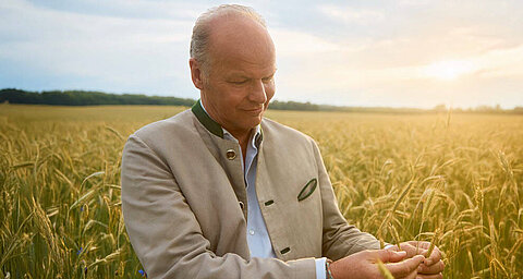A man wearing a beige jacket is checking the wheat stalks in a field.