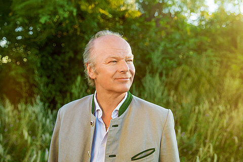 A man wearing a light-coloured jacket is standing outside, looking side to side.