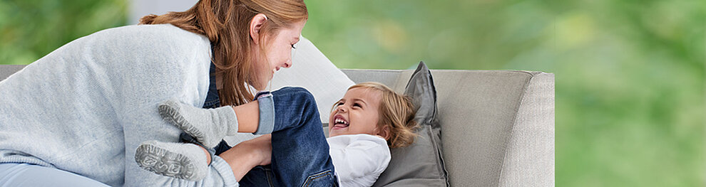 A woman and a child are engaged in a playful interaction on a couch.