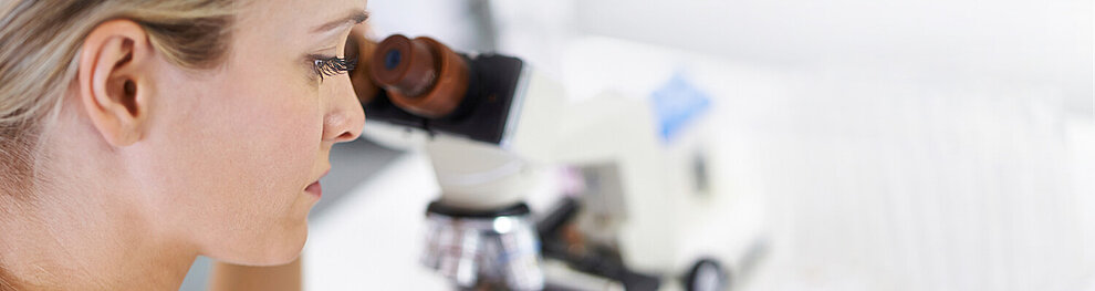 A woman is looking through a microscope.